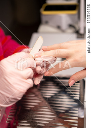 Modern manicure. Nail care. Professional woman manicurist hand in protective gloves client using emery board during beauty procedure. Modern manicure. Nail care. Professional woman manicurist hand in protective gloves client using emery board during beauty procedure. 133514268