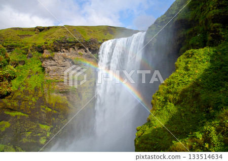 Skógarfoss waterfall flowing down the Skógár River in the Nordic island nation of Iceland, and a rainbow over the waterfall 133514634