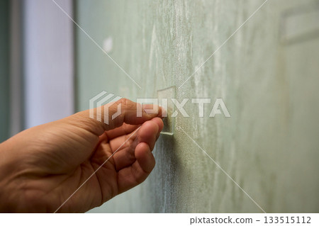 Closeup of textured plaster wall prep, Gently detaching thin tape from wall surface, Homeowner carefully removing adhesive strip to ready wall for repainting process Closeup of textured plaster wall prep, Gently detaching thin tape from wall surface, Homeowner carefully removing adhesive strip to ready wall for repainting process 133515112