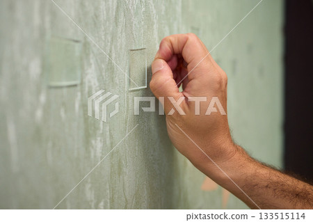 Closeup of textured plaster wall prep, Gently detaching thin tape from wall surface, Homeowner carefully removing adhesive strip to ready wall for repainting process Closeup of textured plaster wall prep, Gently detaching thin tape from wall surface, Homeowner carefully removing adhesive strip to ready wall for repainting process 133515114
