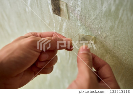 Closeup of textured plaster wall prep, Gently detaching thin tape from wall surface, Homeowner carefully removing adhesive strip to ready wall for repainting process 133515118