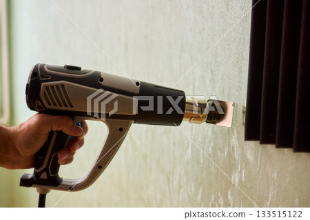 Craftsman carefully detaching acoustic panels indoors, Individual skillfully peels acoustic insulation from wall using heat and precise hand movements for studio setup 133515122