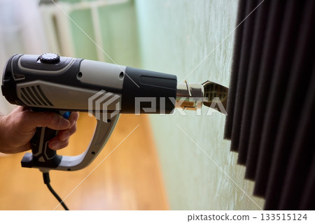 Craftsman carefully detaching acoustic panels indoors, Individual skillfully peels acoustic insulation from wall using heat and precise hand movements for studio setup Craftsman carefully detaching acoustic panels indoors, Individual skillfully peels acoustic insulation from wall using heat and precise hand movements for studio setup 133515124