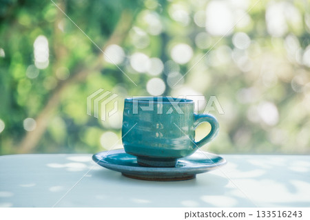 Cafe time with a blue mug against the backdrop of fresh greenery Cafe time with a blue mug against the backdrop of fresh greenery 133516243