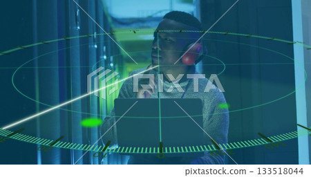 Wearing red headphones, IT technician holding open laptop in server rack aisle, with AR graphics Wearing red headphones, IT technician holding open laptop in server rack aisle, with AR graphics 133518044