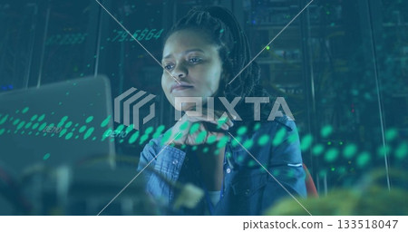 Monitoring woman wearing denim shirt analyzing system on laptop in server room, with blinking racks 133518047