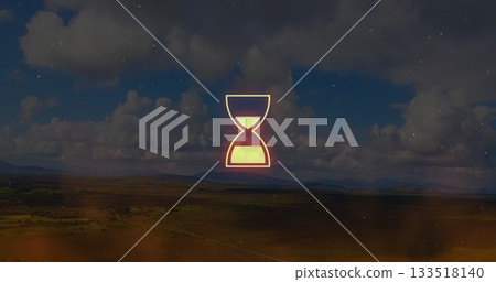 Glowing neon hourglass hovering above fields and hills under cumulus clouds, with particle overlay 133518140