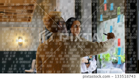 Collaborating professionals writing on glass board in open-plan office, with sticky notes Collaborating professionals writing on glass board in open-plan office, with sticky notes 133518743
