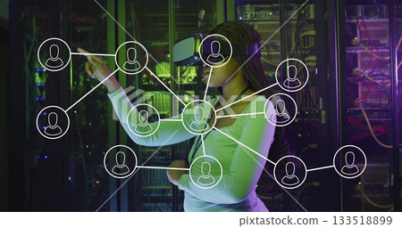 Standing Black woman touching floating network-connection overlay in server room, with VR headset Standing Black woman touching floating network-connection overlay in server room, with VR headset 133518899