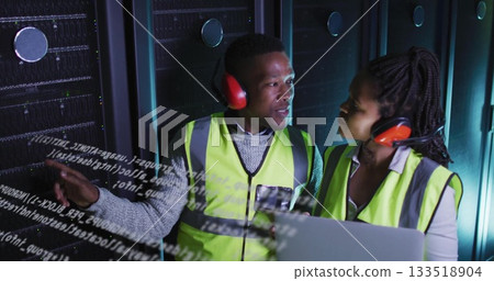 Pointing technicians explaining code overlay at data center racks, with laptop and red headsets 133518904