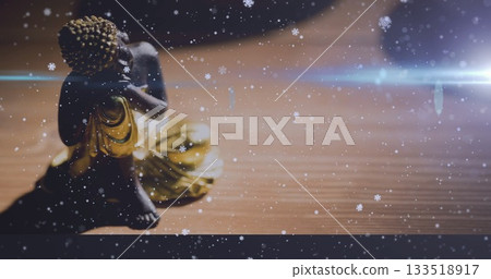 Resting meditative statue wearing golden robe on wooden tabletop with snowflake overlay, lens flare 133518917