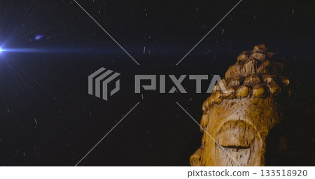 Highlighting Buddha head sculpture in light beam at night showing raindrops, lens flare, copy space 133518920