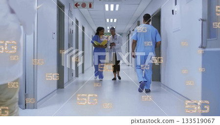 Staff walking in hospital corridor, holding yellow chart, using device and wearing stethoscope Staff walking in hospital corridor, holding yellow chart, using device and wearing stethoscope 133519067