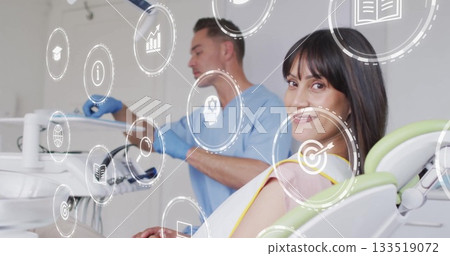 Smiling female patient reclining on chair in clinic room, with tray and digital icons, copy space 133519072