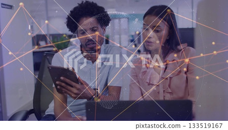 Two professionals viewing tablet and pointing at laptop in modern office, network map 133519167