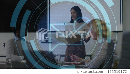 Presenting woman in blouse and skirt discussing report at conference table, with folder and screen 133519172