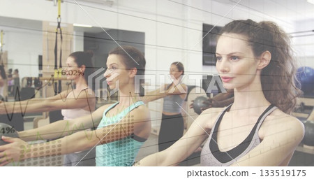 Extending arms forward, six women holding posture in studio, with suspension straps and wall mirror 133519175