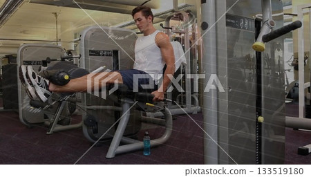 Extending legs adult male gym-goer using leg extension machine in fitness center, with water bottle Extending legs adult male gym-goer using leg extension machine in fitness center, with water bottle 133519180