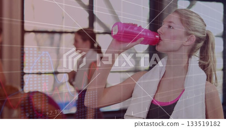 Drinking woman in black sports top with towel in gym, holding pink water bottle, copy space 133519182