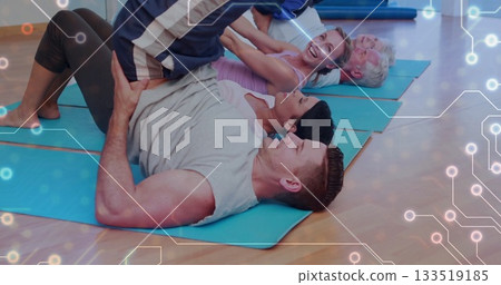 Guiding blue tracksuit instructor helping participant lifting legs in workout studio with blue mats 133519185