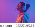 A young girl with her eyes closed enjoys music through headphones. Purple neon background 133519584