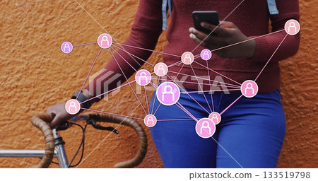Leaning woman holding smartphone against urban orange wall with bicycle and network overlay 133519798