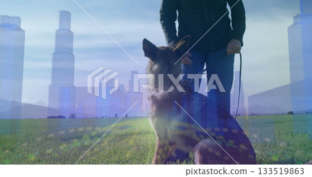 Holding leash wearing jeans and jacket standing behind German Shepherd on grassy field with skyline 133519863