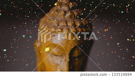 Carved wooden Buddha head statue sitting in studio, with multicolored confetti floating around Carved wooden Buddha head statue sitting in studio, with multicolored confetti floating around 133519894