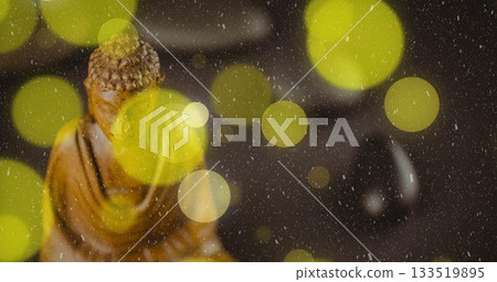 Glowing yellow lights drifting on table beside carved wooden Buddha statue, black polished pebble Glowing yellow lights drifting on table beside carved wooden Buddha statue, black polished pebble 133519895