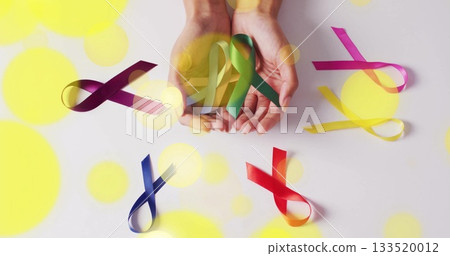 Adult woman hands holding assorted awareness ribbons on white surface, with yellow bokeh flares Adult woman hands holding assorted awareness ribbons on white surface, with yellow bokeh flares 133520012