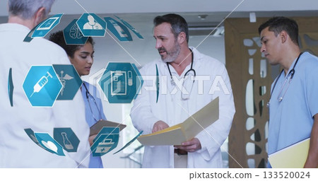Medical team discussing chart in hospital hallway, with white coats, manila folder and stethoscopes 133520024