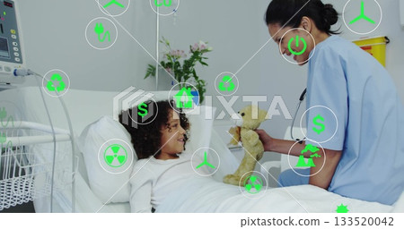 Kneeling nurse offering teddy bear to child patient in pediatric hospital room, with IV pole 133520042