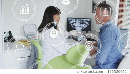 Dentist in lab coat and gloves consulting patient in clinic, with digital icons and X-ray monitor Dentist in lab coat and gloves consulting patient in clinic, with digital icons and X-ray monitor 133520051
