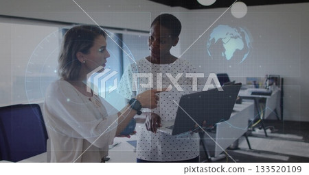 Analyzing two colleagues interacting over laptop in office, with world map and chart overlays 133520109