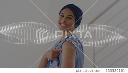 Smiling medical worker in scrubs and turban pointing to vaccine bandage at clinic hall, stethoscope 133520161