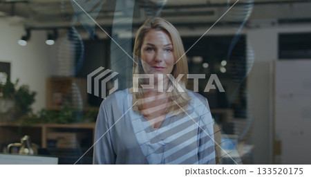 Standing mature businesswoman wearing blue blouse in open-plan office with DNA helix overlay 133520175