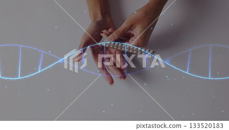 Holding female hands holding blister pack pills over pale gray bench with digital DNA helix graphic Holding female hands holding blister pack pills over pale gray bench with digital DNA helix graphic 133520183