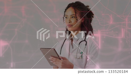 Standing doctor in lab coat holding tablet and stethoscope in studio, reviewing data, copy space 133520184
