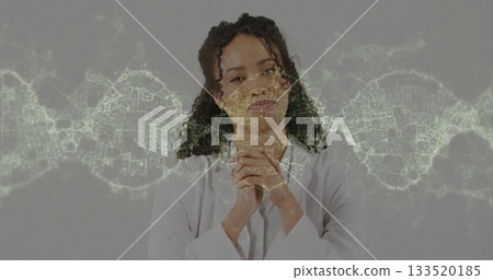 Analyzing digital DNA helix overlay, scientist wearing lab coat clasping hands near chin in studio 133520185