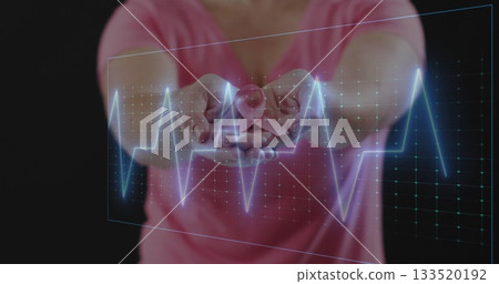 Holding mid adult woman extending hands forward displaying pink ribbon with ECG overlay in studio 133520192