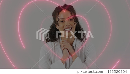 Smiling woman wearing white lab coat standing in professional studio, with neon pink heart graphics 133520204