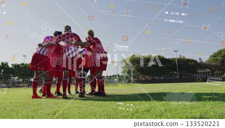 Huddling eight soccer players wearing red jerseys on grass pitch, with soccer ball and goal net Huddling eight soccer players wearing red jerseys on grass pitch, with soccer ball and goal net 133520221