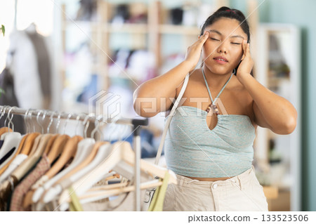 Female shopper suffers from headache while shopping at clothing store Female shopper suffers from headache while shopping at clothing store 133523506