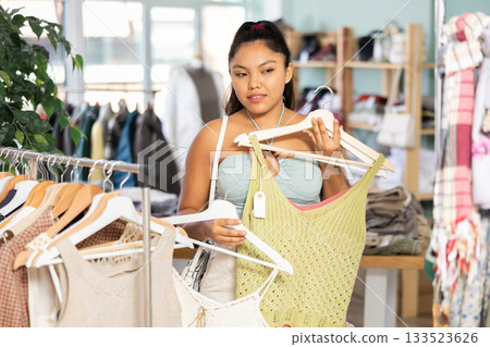 Woman chooses dresses or o tops for the summer period in fashionable clothing store Woman chooses dresses or o tops for the summer period in fashionable clothing store 133523626