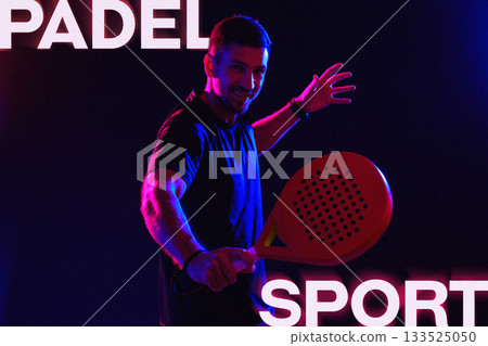 Man enjoying padel sport with a racket in vibrant lighting setting 133525050