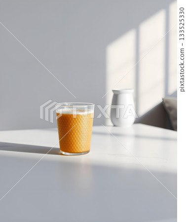 A refreshing glass of orange juice stands on a white table, illuminated by sunlight. 133525330
