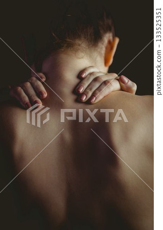 Woman is showing bare upper back clasping hands on neck in painting with featureless dark backdrop Woman is showing bare upper back clasping hands on neck in painting with featureless dark backdrop 133525351