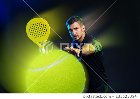 Man playing paddle tennis with a vibrant yellow ball illuminated under studio lights 133525354