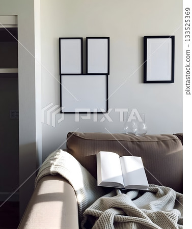 Cozy living room scene with open book, blanket, and framed artwork on the wall. 133525369