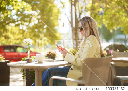 Woman enjoying a sunny afternoon at a cafe while using her smartphone 133525482